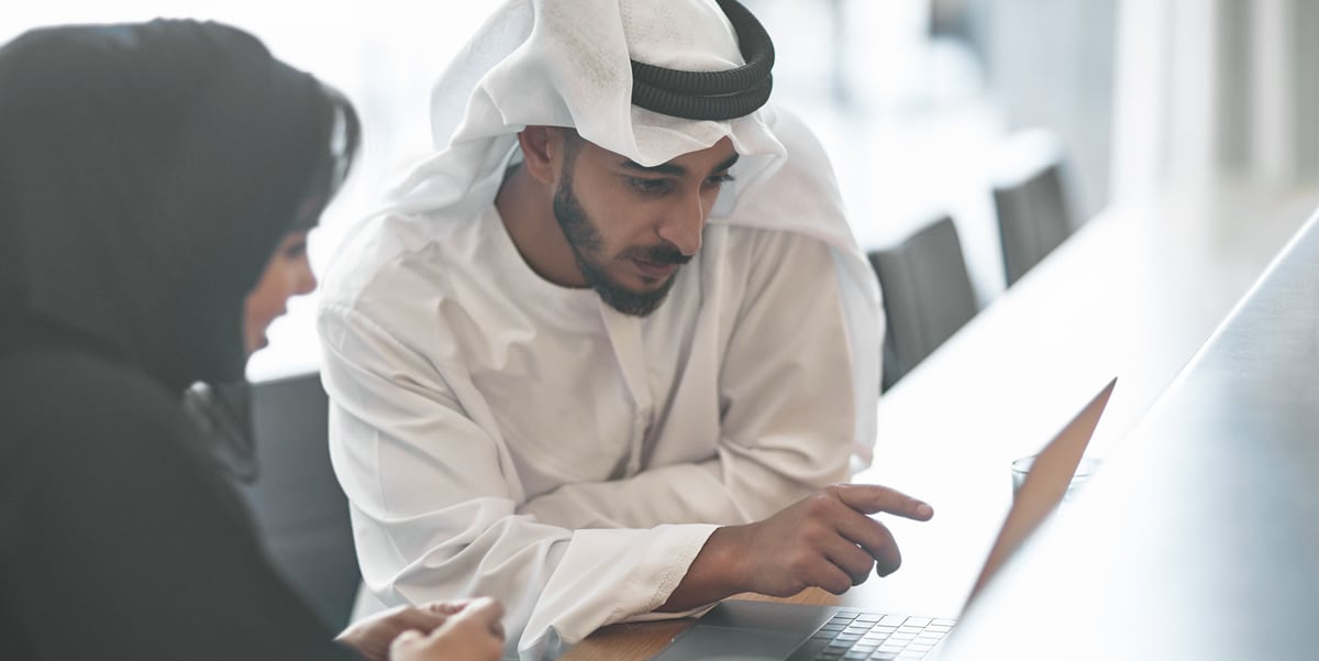 A man and woman wearing abaya are sitting at a table looking at a laptop screen