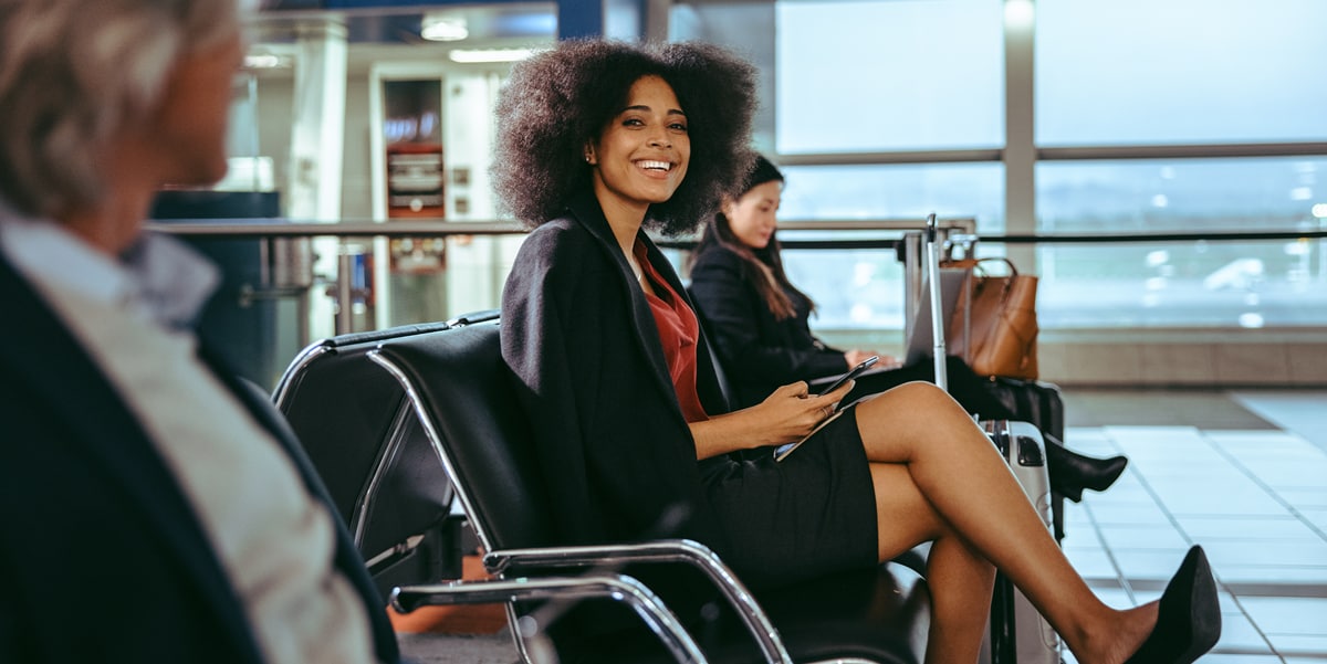 Smiling woman holding a phone sitting at an airport in between two other travellers