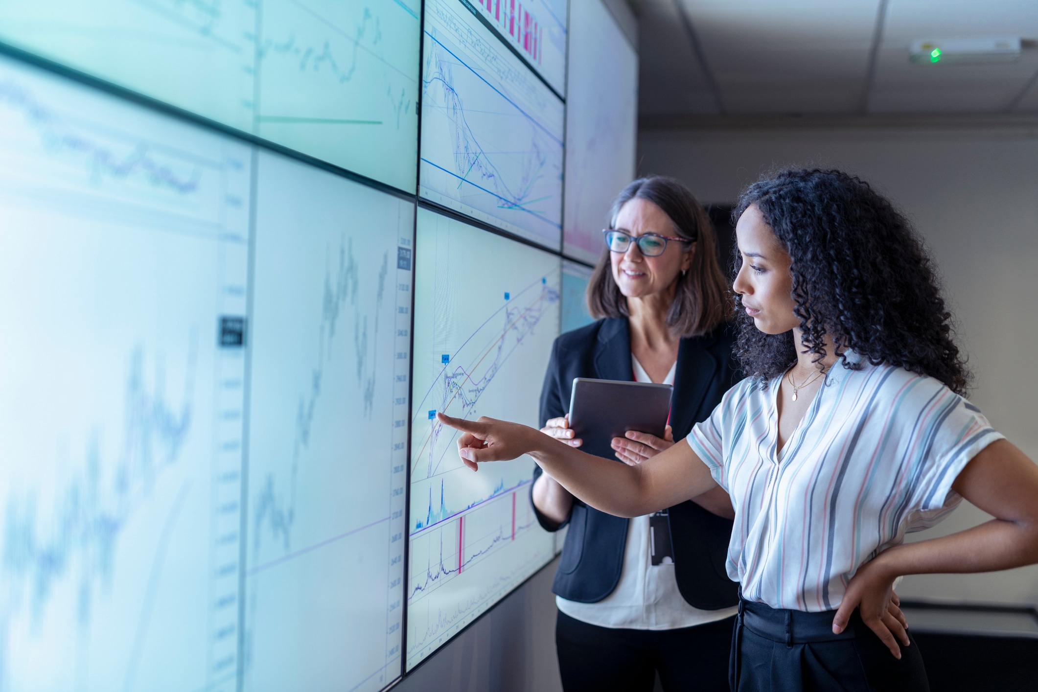 One woman pointing at giant screen and another woman with clipboard next to her