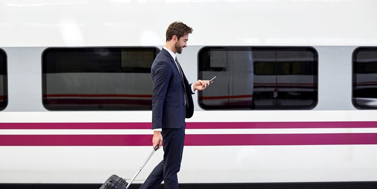 professional man, traveller, standing in front of train, looking at phone